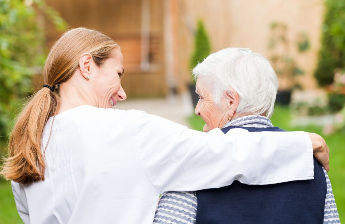 A smiling woman with her arm around the shoulders of an elderly woman.