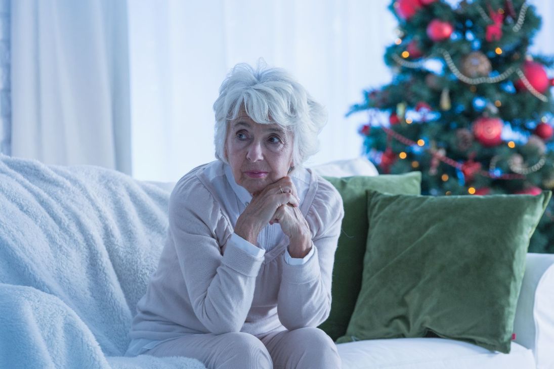 Senior woman sitting alone by Christmas tree.